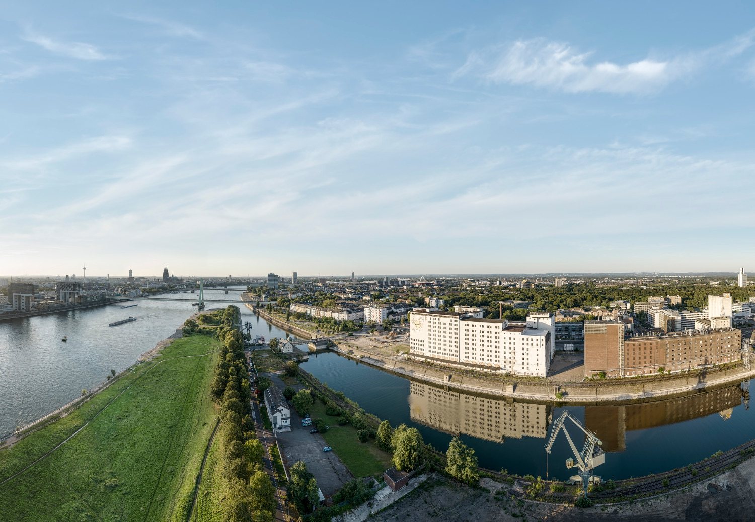 Luftbild des Deutzer Hafens am Abend: Hafenbecken mit Mühlen und Kran, Poller Wiesen, Rhein mit Severinsbrücke, im Hintergrund Dom und Kölner Innenstadt